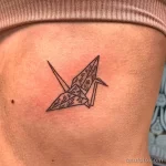 Фото тату: минималистичный рисунок оригами журавля на теле. Черные контуры, геометрический стиль, простота и элегантность.
