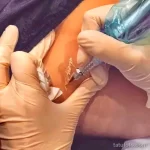 Фото процесса создания татуировки: мастер в перчатках наносит рисунок на кожу с помощью тату-машинки. Кадр демонстрирует профессиональный подход и внимание к деталям.