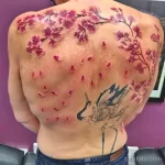 Фото тату аиста и цветущей сакуры на спине. Черно-серый рисунок с использованием акварельной техники и нежных оттенков.