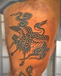 Фото тату аиста в японском стиле на бедре. Черно-серый рисунок с детальной проработкой перьев и волн.