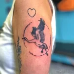 Фото тату серого журавля в круге с точками и сердечком на плече. Мягкие тона и минималистичный дизайн. Идеальный эскиз тату для романтичных натур.