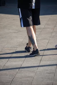 Крупный план татуировки на икре мужчины, выполненной в технике blackwork. Видны детализированные элементы пейзажа.