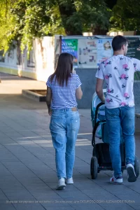 Фото тату на руке женщины, идущей с мужем и ребенком в коляске по городской улице. Рисунок татуировки выполнен в черном цвете и частично виден из-под рукава.