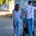 Фото тату на руке женщины, идущей с мужем и ребенком в коляске по городской улице. Рисунок татуировки выполнен в черном цвете и частично виден из-под рукава.
