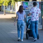 Фото тату на руке женщины, идущей с мужем и ребенком в коляске по городской улице. Рисунок татуировки выполнен в черном цвете и частично виден из-под рукава.