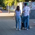 Фото тату на руке женщины, идущей с мужем и ребенком в коляске по городской улице. Рисунок татуировки выполнен в черном цвете и частично виден из-под рукава.