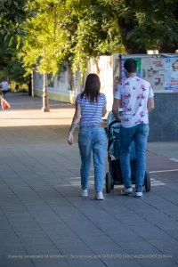 Фото тату на руке женщины, идущей с мужем и ребенком в коляске по городской улице. Рисунок татуировки выполнен в черном цвете и частично виден из-под рукава.