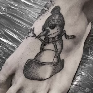 Фото тату с изображением снеговика в шапке и шарфе, выполненное в стиле blackwork. Рисунок имеет минималистичный дизайн и выполнен полностью в черном цвете.