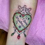 Фото тату на руке с изображением сердца, украшенного снежинкой и надписью 'I love Christmas'. Яркий и красочный рисунок татуировки в праздничном стиле.