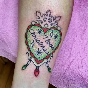 Фото тату на руке с изображением сердца, украшенного снежинкой и надписью 'I love Christmas'. Яркий и красочный рисунок татуировки в праздничном стиле.