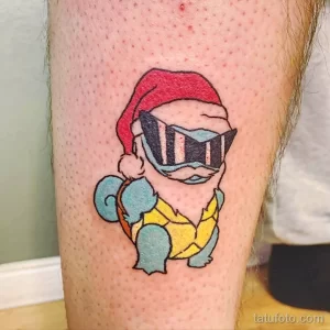 Фото тату Squirtle из Pokemon в красной шапке и очках на ноге. Яркий и мультяшный рисунок татуировки.