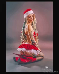 Фотография девушки в костюме Санты, демонстрирующая татуировки на плече и боку. Яркий образ и детализированные тату привлекают внимание.