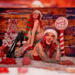 Фото тату двух девушек в костюмах эльфов, позирующих на фоне рождественских декораций. Яркий и красочный рисунок татуировки.