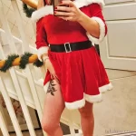 Фотография девушки в красном костюме Санты, с татуировками на ноге, делающей селфи в зеркале.