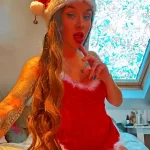 Фотография девушки в шапке Санты и красном платье, демонстрирующая татуировку на руке. Яркий макияж и праздничная атмосфера.