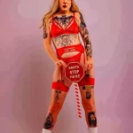Фото тату на теле девушки в красном костюме Санты. Множество татуировок, вызывающий взгляд и табличка "SANTA STOP HERE".