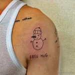 Простое тату снеговика на плече с надписью 'Free Hug', выполненное в минималистичном стиле черными линиями.