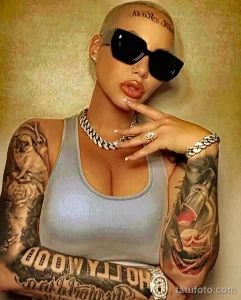 Фото тату: Amber Rose с татуировками на руках, включая изображения ангелов, роз и надпись "Good Luck Charm". Иллюстрация для поиска идей тату в стиле full sleeve.