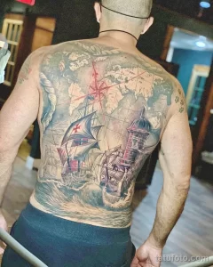 Фото тату морской тематики на спине. Детализированный черно-серый рисунок с кораблем, маяком, картой мира и морскими волнами, создающий атмосферу приключений.