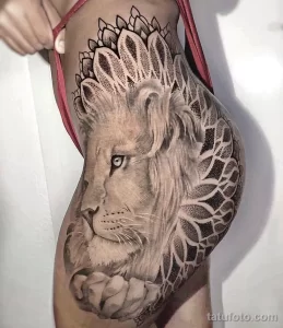 Фото тату: реалистичное изображение головы льва с мандалой на бедре. Черно-серые тона, детализированный рисунок, эффектное сочетание символов.