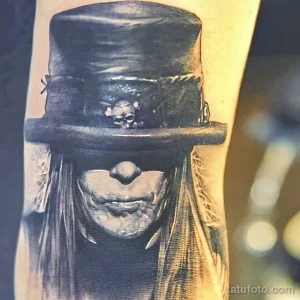 Фото тату с изображением Слэша, гитариста Guns N' Roses, в его фирменном цилиндре. Детализированный портрет в черно-белой гамме на руке.