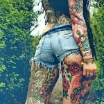 Фото тату: женские бедра и ноги, украшенные яркими татуировками в традиционном стиле. Изображены розы, птицы, матросы и другие символы.