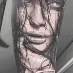Фото тату: реалистичный портрет женщины с распущенными волосами и розой в руке, выполненный в черно-серых тонах на плече.