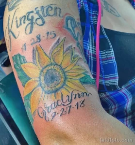 Фото яркой татуировки на руке с изображением подсолнуха и имен 'Kingston' и 'Graclynn' с датами. Татуировка выполнена в ярких цветах, создающих красочный рисунок.