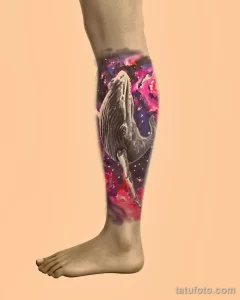 Цветная татуировка кита, плывущего в космосе, на икре. Детализированный рисунок татуировки с использованием ярких цветов и эффекта акварели.