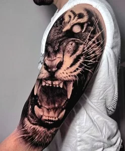 Фото тату тигра на руке, выполненное в реалистичном стиле. Крупный план рычащей головы тигра с детализированной проработкой шерсти и глаз.