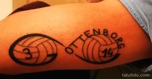 Фото татуировки на плече с двумя волейбольными мячами и надписью "OTTENBORG 14". Рисунок выполнен в черном цвете, с четкими линиями и цифрами.