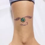Фото тату на лодыжке: изображение золотого снитча из Гарри Поттера с подписью "Mimi", выполненное в акварельном стиле с использованием ярких цветов.