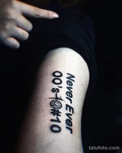 Фото тату с изображением волейбольного мяча и надписью 'Never Ever 00's 10', выполненного на руке в черном цвете.