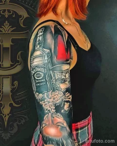 Фото тату: впечатляющая татуировка на руке, изображающая бутылку Jack Daniel's и череп. Реалистичный эскиз тату для любителей виски и рока.