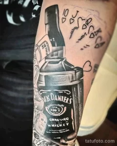 Фото тату бутылки Jack Daniel's с сердечками и надписями, выполненное в смешанном стиле. Оригинальный и эмоциональный рисунок татуировки на руке.