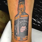 Черно-серая татуировка на руке с изображением бутылки Jack Daniel's. Детализированный рисунок татуировки с реалистичной прорисовкой этикетки.