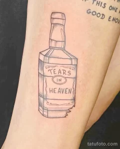 Фото минималистичной татуировки на руке: контурный рисунок бутылки с надписью "TEARS IN HEAVEN". Простой и элегантный дизайн татуировки.
