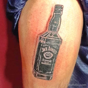 Фото татуировки на руке с изображением бутылки виски Jack Daniel's, выполненной в черно-белой гамме с точками.