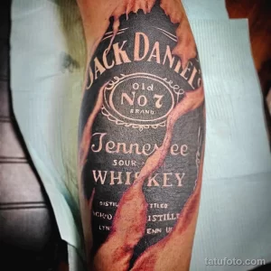 Фото тату крупной этикетки виски Jack Daniel's на руке. Черно-белый рисунок с детализированной проработкой текста и логотипа.