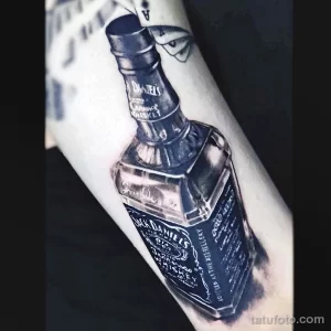 Фото монохромной татуировки бутылки Jack Daniel's на руке. Четкие линии и реалистичное изображение в черно-белой гамме.