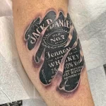 Фото реалистичной татуировки бутылки виски Jack Daniel's на руке. Детализированное изображение с тенями и текстурами.