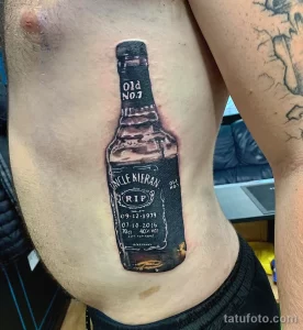 Фото тату на груди с изображением бутылки виски Old No.7 и надписью "Uncle Kieran" с датами рождения и смерти. Памятный рисунок.