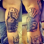 Фото тату на руке с изображением бутылки виски Jack Daniel's, игральных карт, стакана виски и черепов. Реалистичный стиль, темные тона.