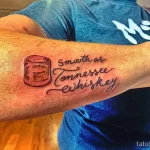 Черно-белая татуировка на руке с изображением стакана виски и надписью 'Smooth as Tennessee whiskey'. Рисунок выполнен в стиле лайнарт.