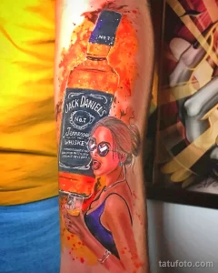 Фото тату на руке: яркая и красочная татуировка с изображением бутылки Jack Daniel's и девушки в стиле пин-ап.
