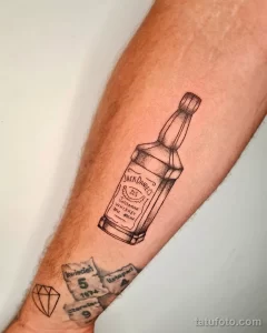 Фото тату на руке: минималистичный контурный рисунок бутылки виски Jack Daniel's, выполненный в черном цвете.