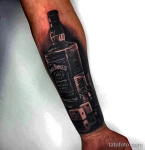 Фото тату на руке: реалистичное изображение бутылки виски Jack Daniel's с игральными костями, выполненное в черно-серых тонах, с акцентом на детали.