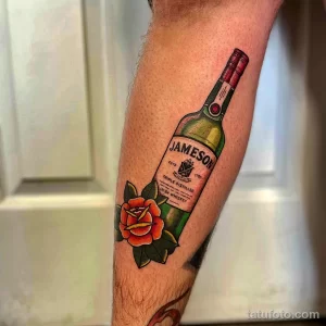 Цветная татуировка бутылки виски Jameson с красной розой, выполненная на ноге. Реалистичный рисунок татуировки с яркими цветами.