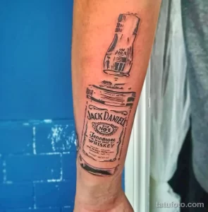 Фото тату на руке: бутылка Jack Daniel's, выполненная в стиле эскиза. Черно-белый рисунок с неровными линиями и эффектом незаконченности.