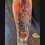 Фото тату реалистичного изображения бутылки Jack Daniel's и стакана виски на руке, выполненного в ярких цветах и с высокой детализацией.